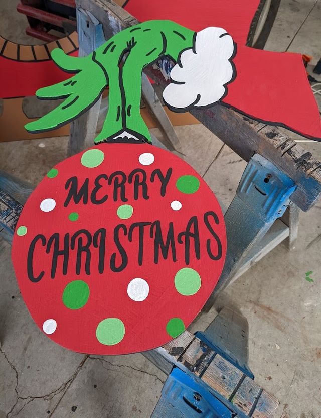 The Grinch's hand holding a Merry Christmas ornament